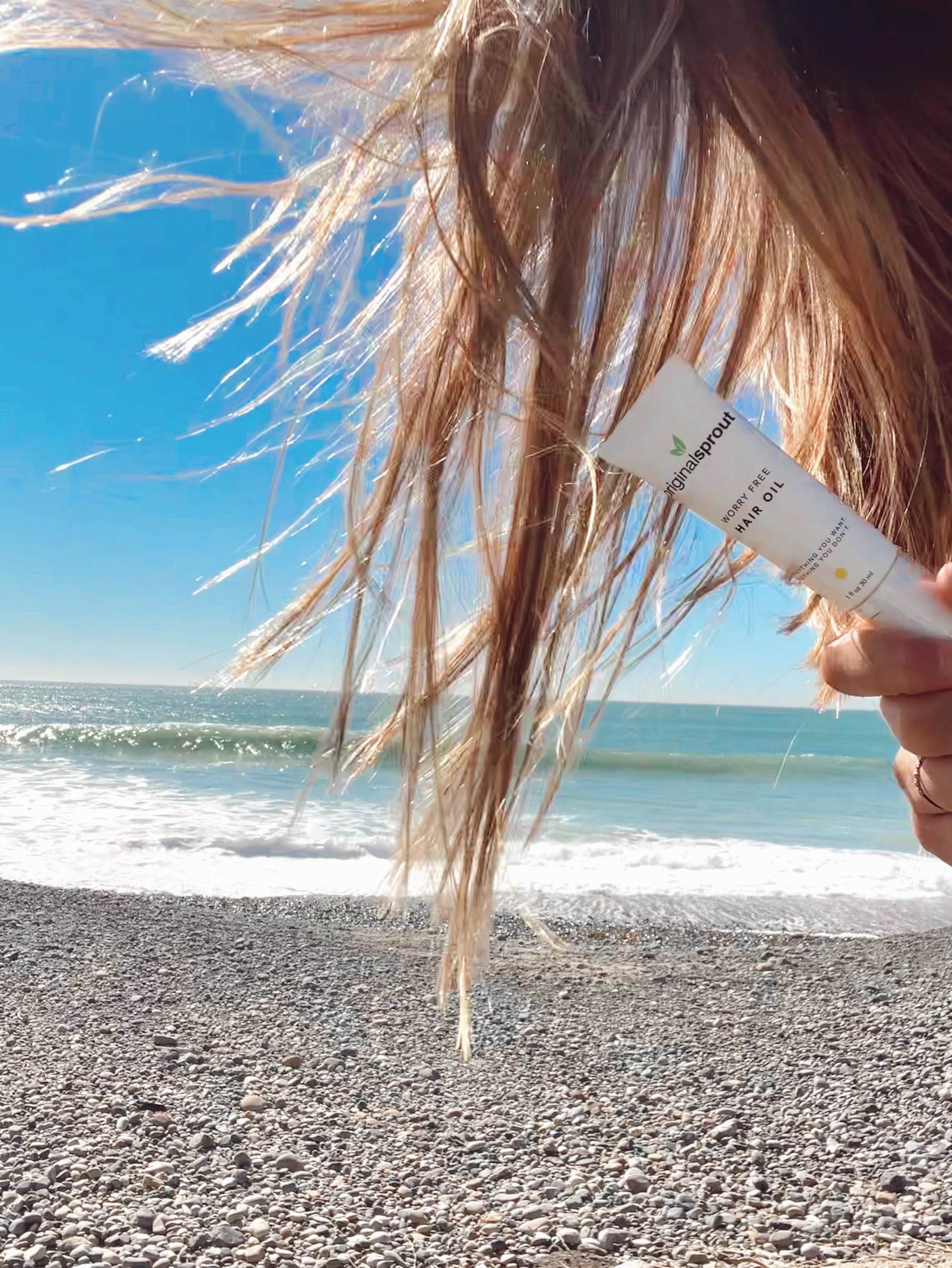 girl holding 4 oz hair oil at beach