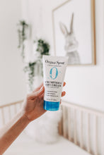 Load image into Gallery viewer, Hand holding a tube of Original Sprout Scrumptious Baby Cream in a blurred room setting